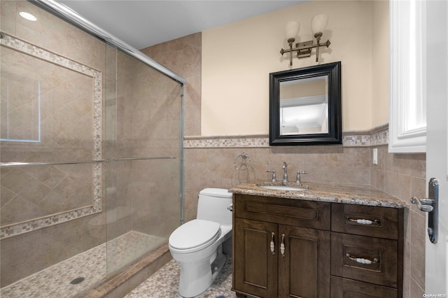 bathroom featuring vanity, toilet, a shower with door, and tile walls