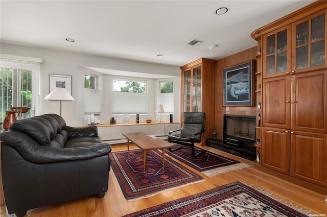 living room with baseboard heating, a tile fireplace, a wealth of natural light, and light wood-type flooring