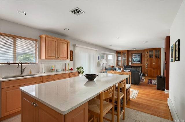 kitchen featuring light wood-type flooring, backsplash, light stone counters, sink, and a center island