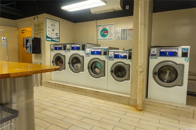 clothes washing area featuring washing machine and dryer, light hardwood / wood-style flooring, and an AC wall unit