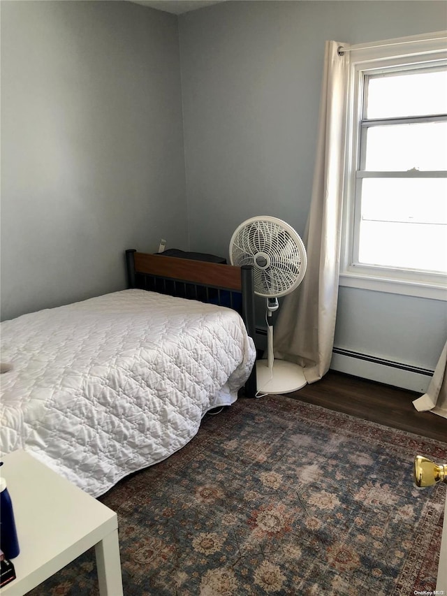 bedroom with dark hardwood / wood-style floors and a baseboard heating unit