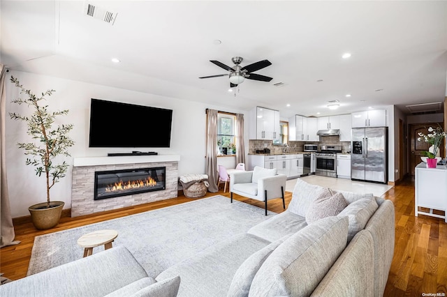 living room with light hardwood / wood-style floors, a stone fireplace, and ceiling fan