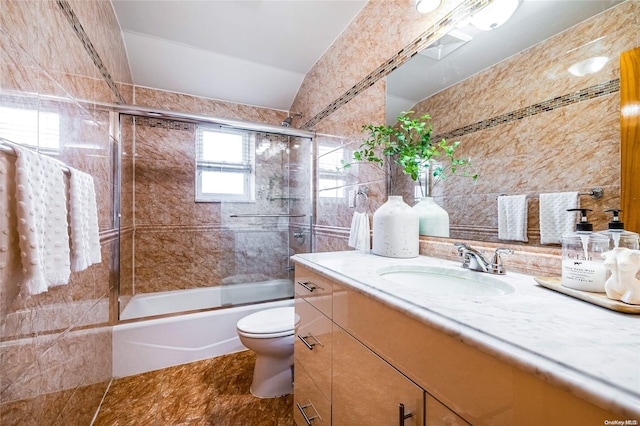 full bathroom featuring vanity, vaulted ceiling, shower / bath combination with glass door, tile walls, and toilet