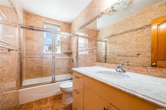 full bathroom with vanity, tile patterned floors, bath / shower combo with glass door, toilet, and tile walls