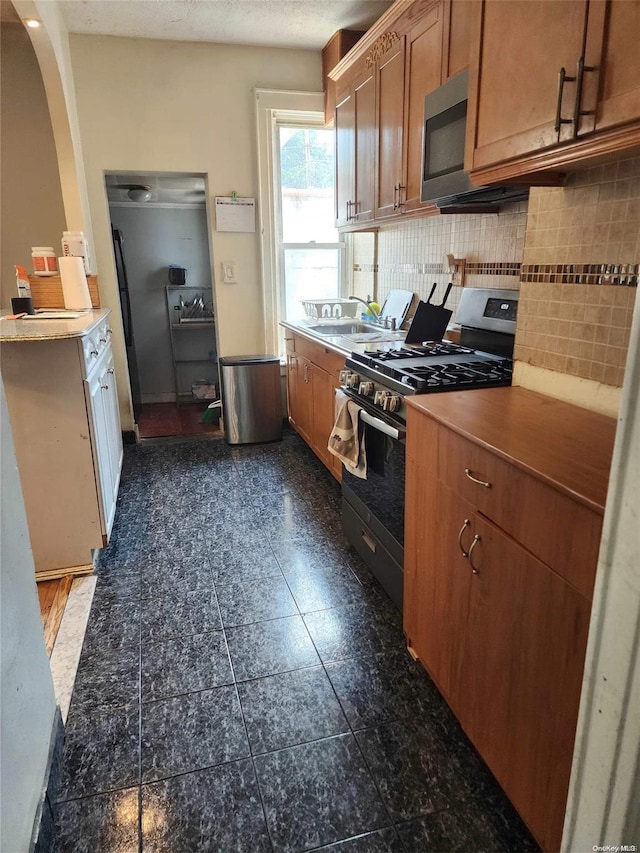 kitchen with sink, decorative backsplash, dark tile patterned floors, a textured ceiling, and appliances with stainless steel finishes