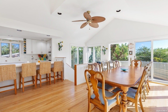 dining room featuring ceiling fan, sink, high vaulted ceiling, and light hardwood / wood-style flooring