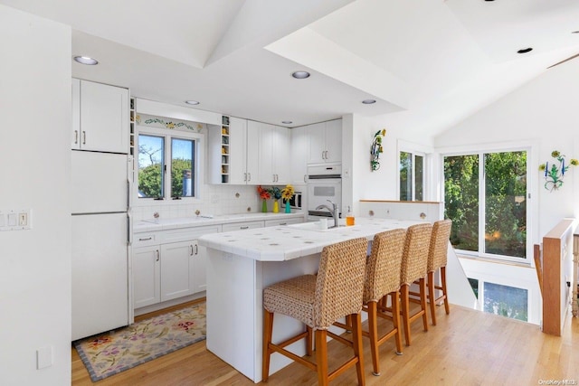 kitchen with white appliances, light hardwood / wood-style flooring, white cabinetry, and a breakfast bar area