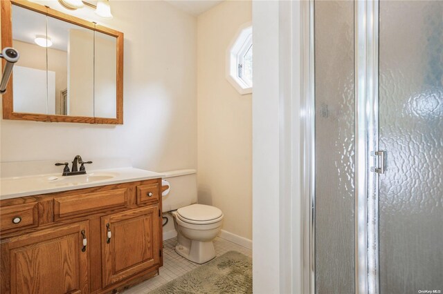bathroom with vanity, a shower stall, toilet, tile patterned floors, and baseboards