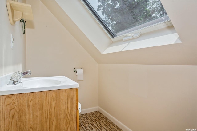 bathroom featuring toilet, vanity, a skylight, baseboards, and lofted ceiling