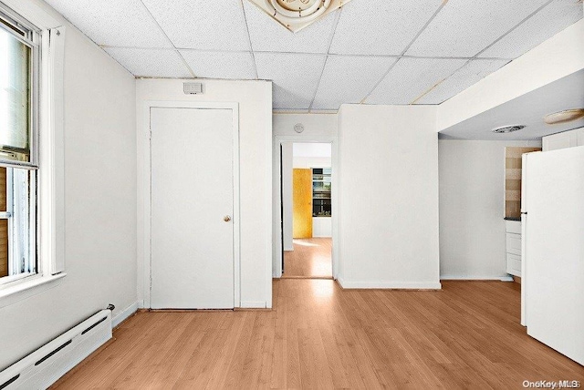 empty room featuring a drop ceiling, light hardwood / wood-style floors, and baseboard heating