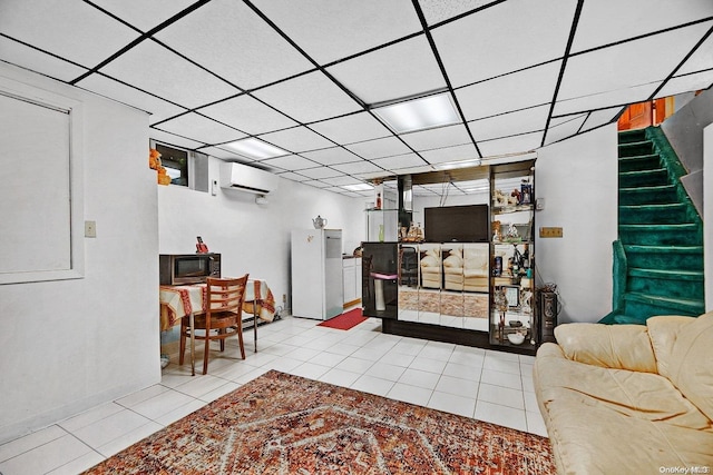 living room with a wall mounted air conditioner, a drop ceiling, and light tile patterned flooring