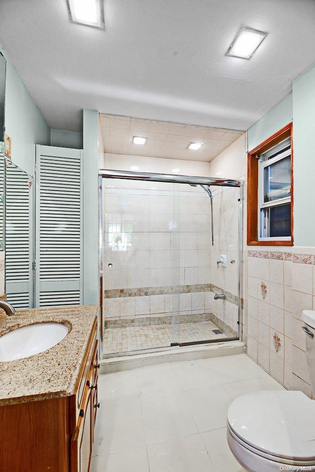 bathroom featuring a textured ceiling, an enclosed shower, toilet, vanity, and tile walls