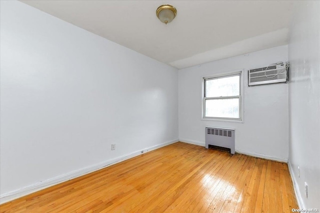 spare room with radiator heating unit, light hardwood / wood-style floors, and a wall unit AC