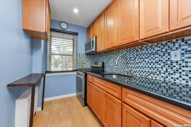 kitchen featuring decorative backsplash, stainless steel appliances, sink, light hardwood / wood-style flooring, and dark stone countertops