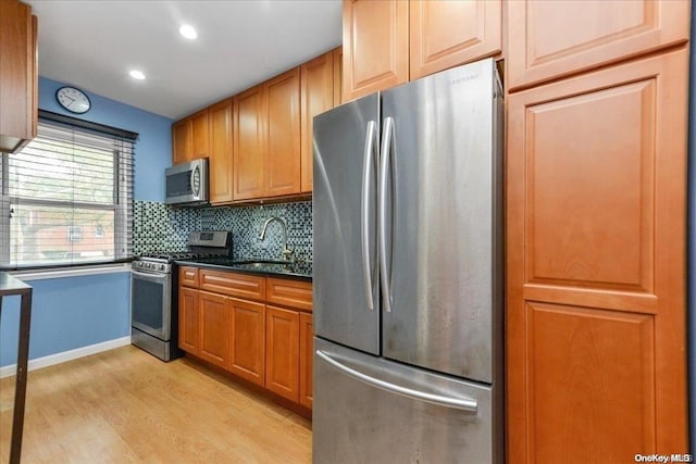 kitchen with tasteful backsplash, sink, appliances with stainless steel finishes, and light hardwood / wood-style flooring