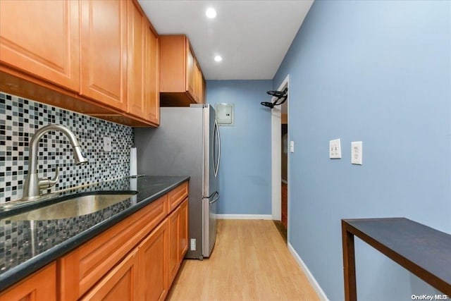 kitchen featuring sink, light hardwood / wood-style flooring, dark stone countertops, tasteful backsplash, and stainless steel refrigerator