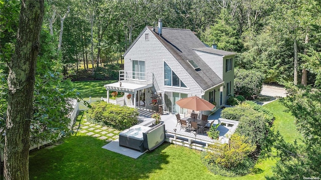 rear view of house with a balcony, a hot tub, a deck, and a lawn