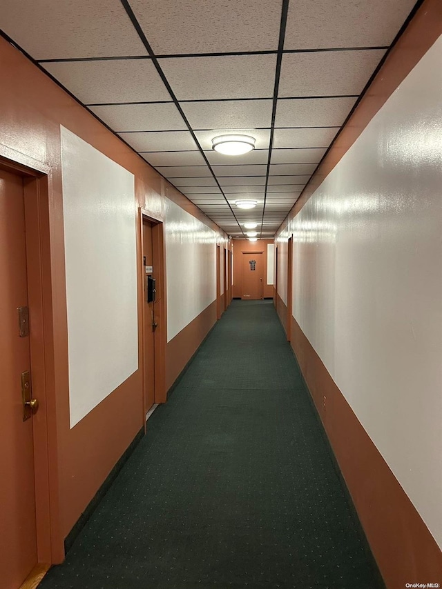 hallway with dark colored carpet and a paneled ceiling