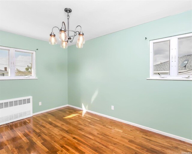 spare room featuring hardwood / wood-style floors, radiator heating unit, and an inviting chandelier