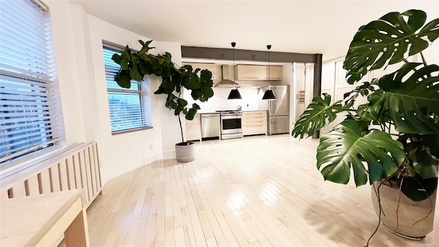 kitchen featuring decorative light fixtures, light hardwood / wood-style floors, wall chimney range hood, and appliances with stainless steel finishes