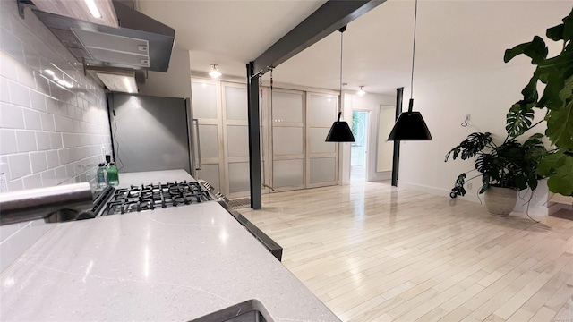 kitchen with hanging light fixtures, stainless steel fridge, light stone countertops, light hardwood / wood-style floors, and extractor fan