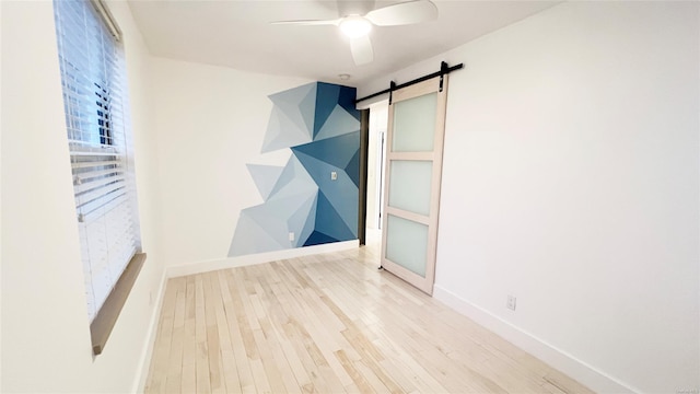 empty room with a barn door, ceiling fan, and light hardwood / wood-style floors