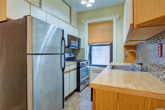 kitchen with radiator, sink, decorative backsplash, white cabinetry, and stainless steel appliances