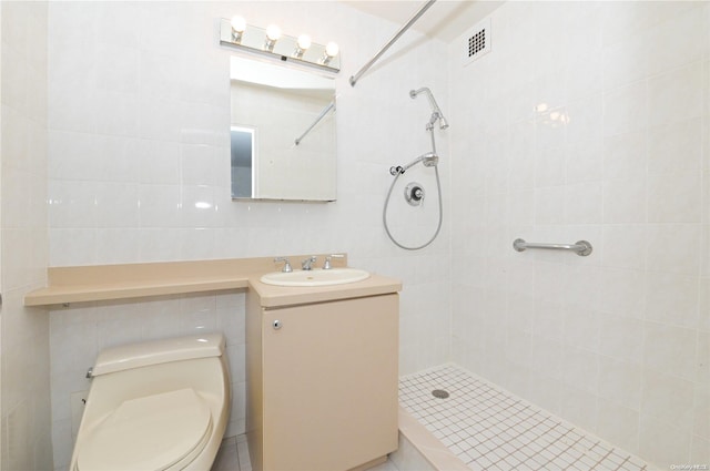 bathroom with vanity, toilet, tile walls, and a tile shower