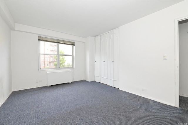 spare room featuring dark carpet and radiator