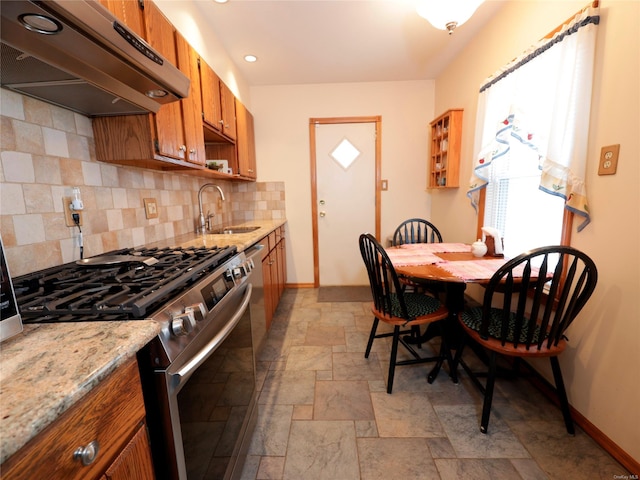 kitchen featuring sink, tasteful backsplash, light stone counters, range hood, and stainless steel stove