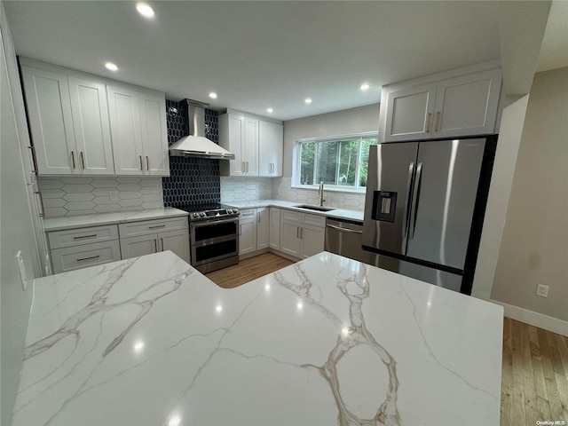 kitchen with light stone countertops, light wood-type flooring, wall chimney exhaust hood, stainless steel appliances, and white cabinets