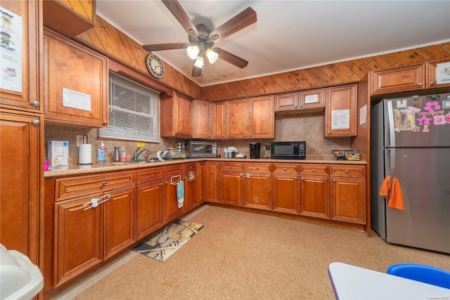 kitchen featuring stainless steel refrigerator, wood walls, sink, and ceiling fan