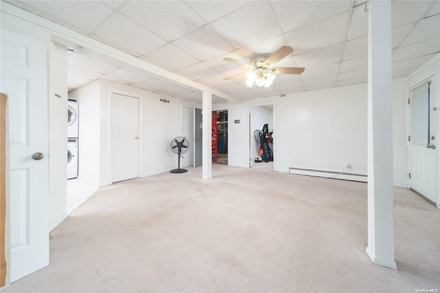 basement with a drop ceiling, light colored carpet, baseboard heating, and stacked washer and dryer