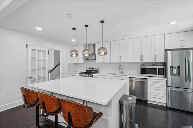 kitchen featuring pendant lighting, wall chimney range hood, sink, appliances with stainless steel finishes, and white cabinetry