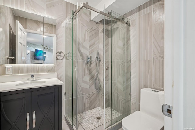 bathroom with vanity, toilet, a shower with shower door, and tile walls