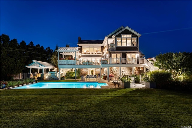 back house at night featuring a lawn, a patio area, and a balcony