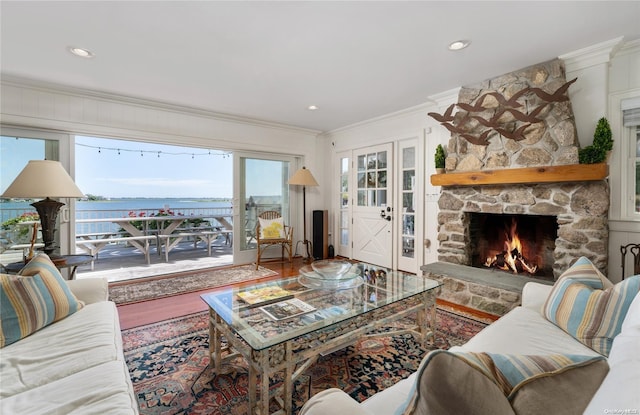 living room with a stone fireplace, crown molding, a water view, and hardwood / wood-style flooring