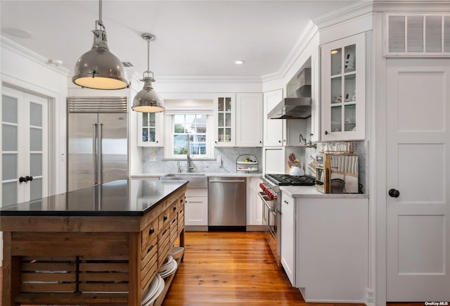 kitchen with white cabinetry, wall chimney exhaust hood, premium appliances, light hardwood / wood-style flooring, and pendant lighting