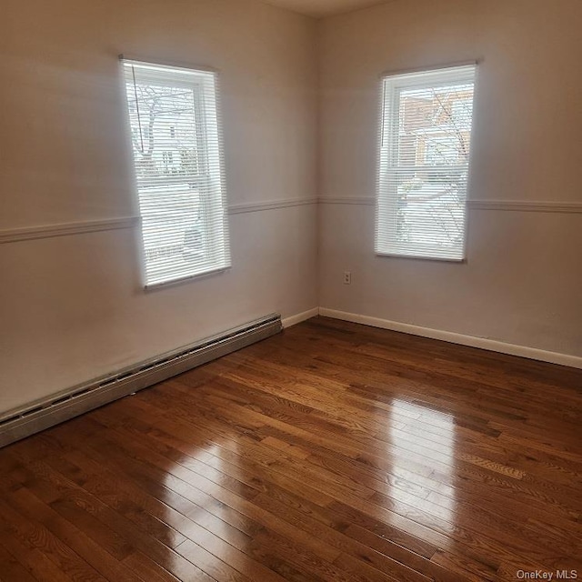 unfurnished room with a baseboard heating unit and dark hardwood / wood-style floors