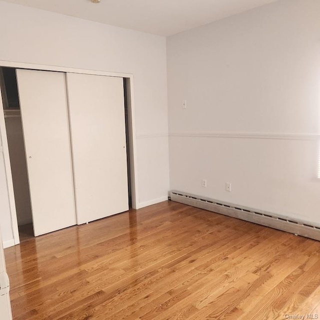 unfurnished bedroom featuring a baseboard heating unit, light hardwood / wood-style flooring, and a closet