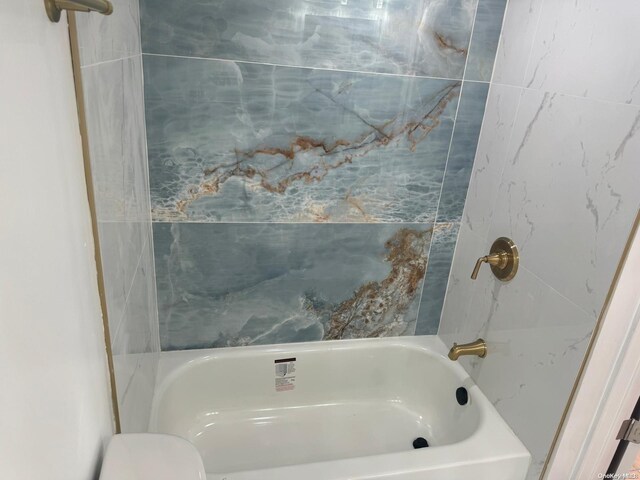 bathroom with tiled shower / bath combo and toilet