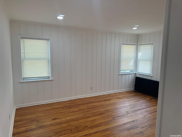 unfurnished room featuring hardwood / wood-style floors, wood walls, radiator heating unit, and crown molding