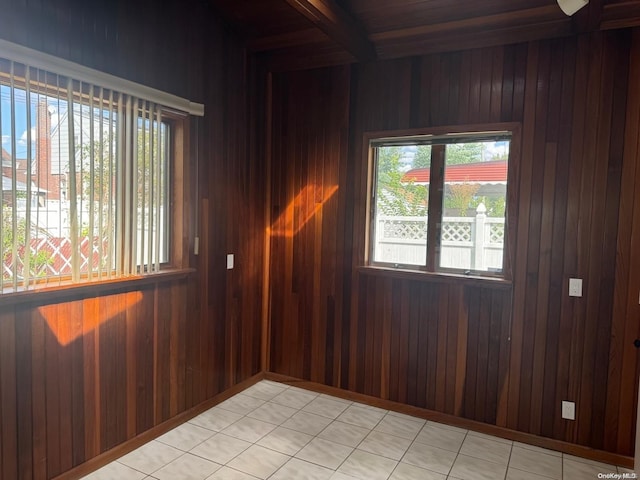 spare room featuring beamed ceiling, light tile patterned flooring, and wooden walls