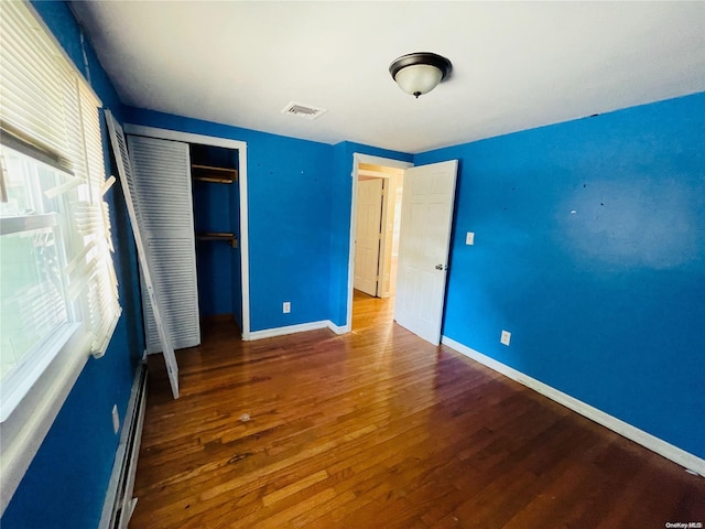 unfurnished bedroom with dark hardwood / wood-style floors, baseboard heating, and a closet