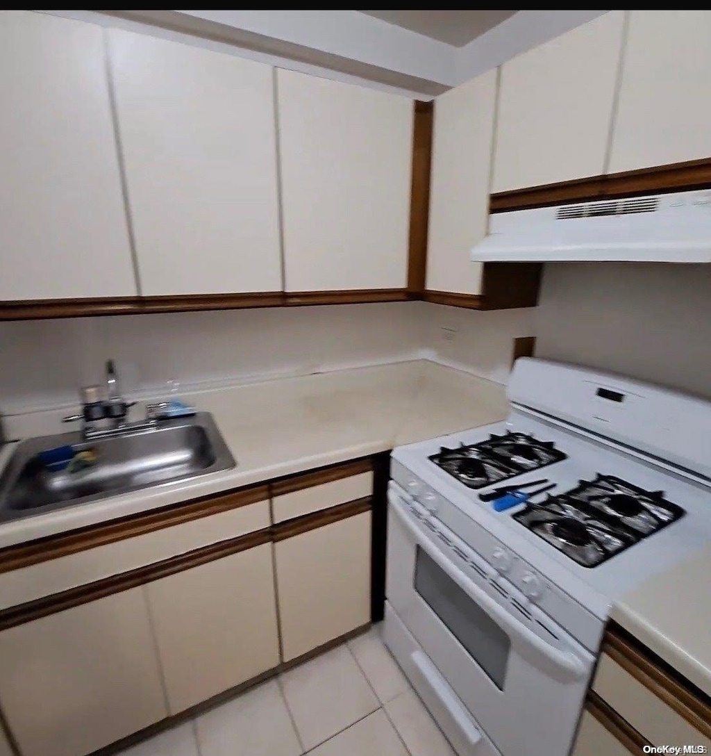 85-15 Main St Unit 12S, Briarwood, NY 11435 - kitchen with white gas stove, under cabinet range hood, white cabinetry, light countertops, and a sink