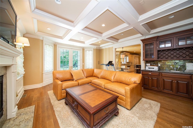 living room with coffered ceiling, ornamental molding, sink, a premium fireplace, and hardwood / wood-style floors