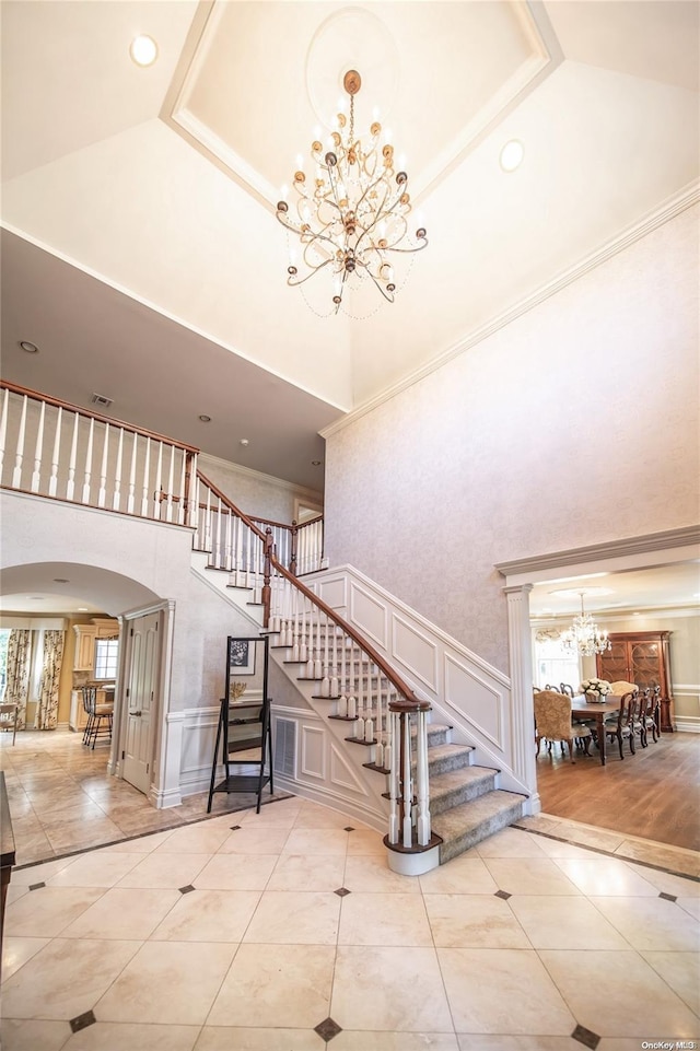 stairs with high vaulted ceiling, crown molding, ornate columns, a notable chandelier, and wood-type flooring