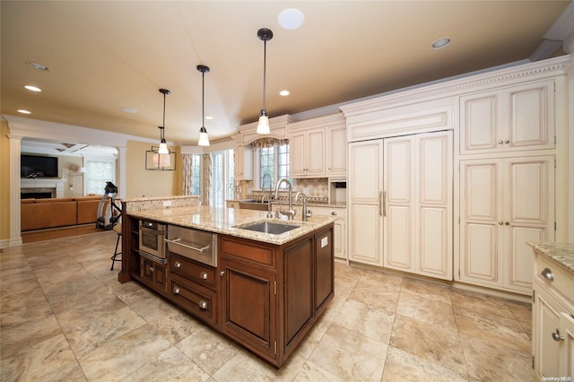 kitchen featuring light stone countertops, a center island with sink, decorative light fixtures, and ornamental molding