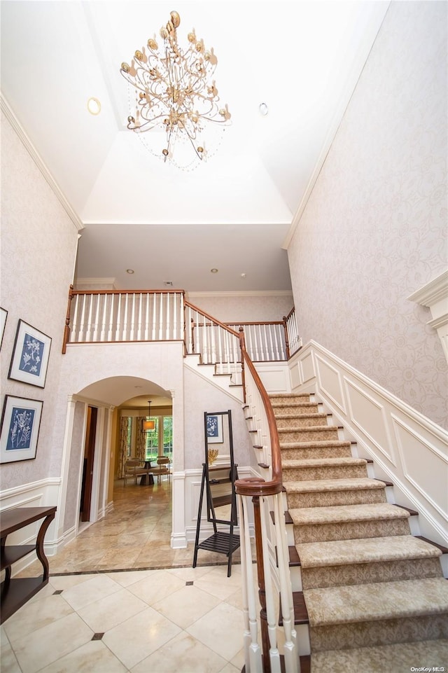 stairway with a towering ceiling, an inviting chandelier, and crown molding