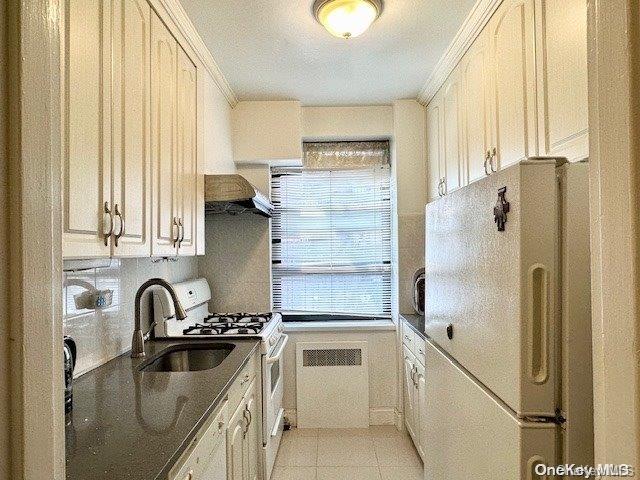 kitchen featuring radiator, ornamental molding, white appliances, sink, and light tile patterned flooring